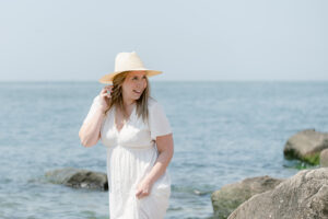 Portrait of a woman wearing a white dress and hat by the water.
