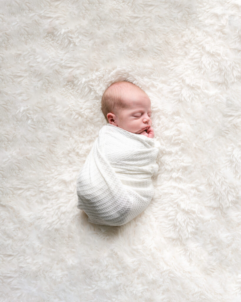 at home newborn photoshoot of baby boy wrapped in a white swaddle